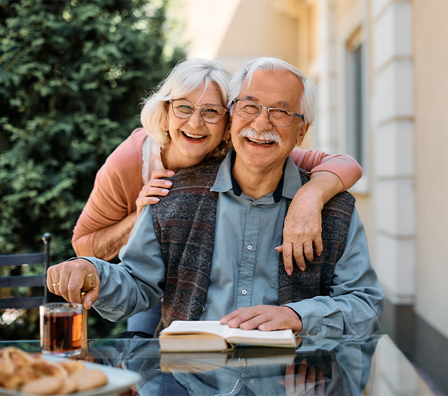 smiling senior couple sitting at table outside reading